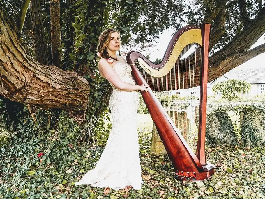 Chloe Chousmer-Kerr in a white lace gown beside her concert harp under an ivy-covered tree