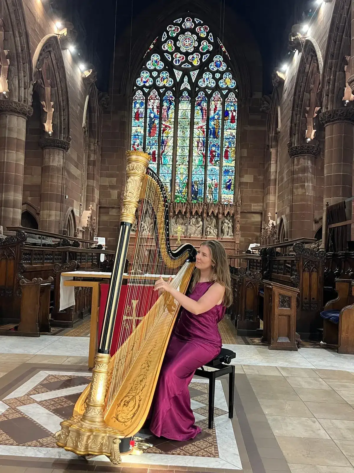 Chloe Chousmer-Kerr playing a gold concert harp in a church in front of a stained-glass window